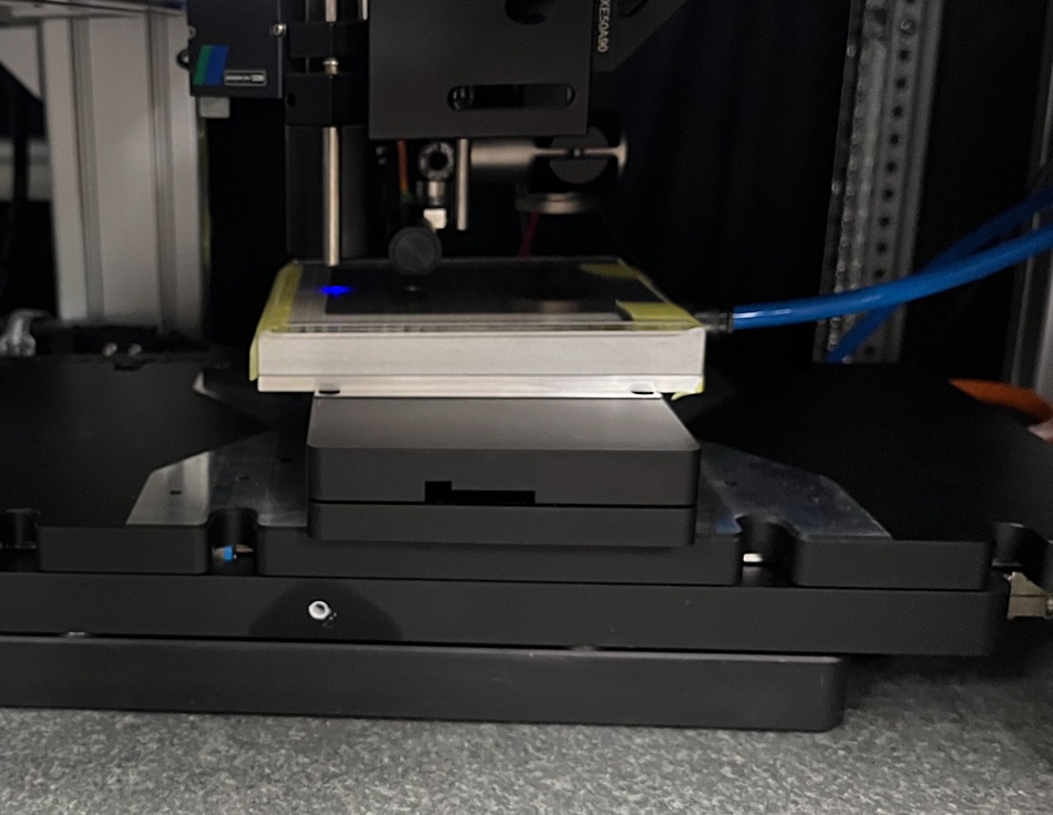 Glass carrier on read/write station platform. The blue light is the femto-second laser beam