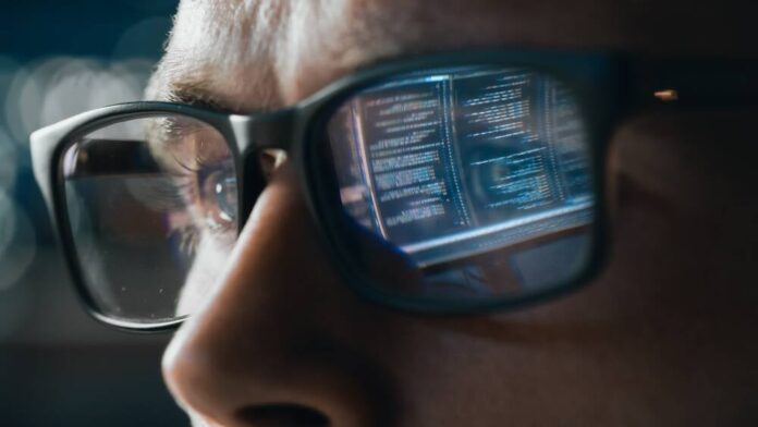 Data reflected in a man's glasses.